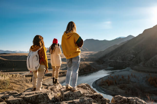 Three female hikers or tourists in sunset mountains Three female tourists or hikers are standing on cliff and looking at sunset river and mountains altai republic photos stock pictures, royalty-free photos & images