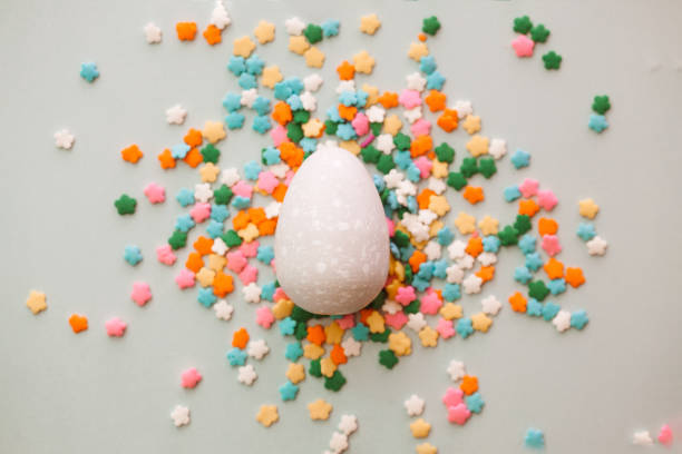 istock White Easter egg on grey background with colourful sprinkles. Yellow, orange, pink, white, blue and green sugar edible decoration  with Easter egg. 1308637720