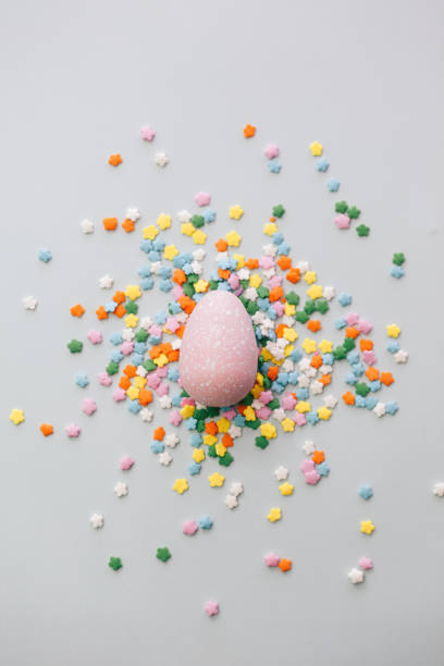 istock Pink Easter egg on light blue background with holiday sprinkles. Easter holiday background. 1308638074