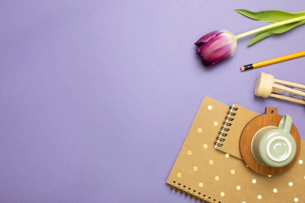 istock Notebook, mug cup, hourglass, tulip, pencil on purple background. flat lay, top view, copy space. Work and study place 1308639489