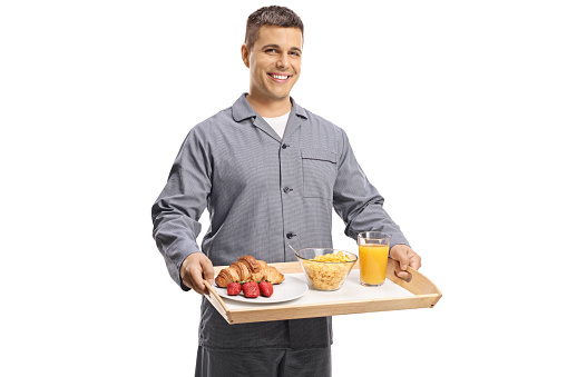 Young man in pajamas holding a breakfast tray isolated on white background