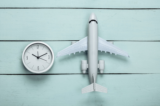 Time to travel. Plane figurine and clock on blue wooden background. Top view. Flat lay