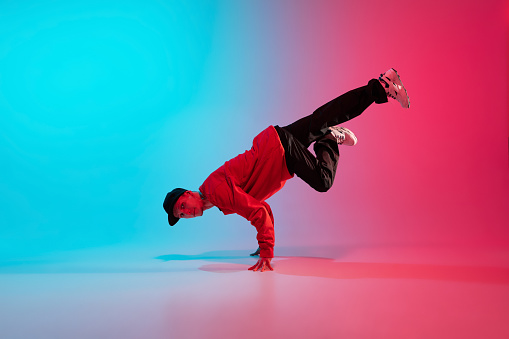 Party. Beautiful sportive boy dancing hip-hop in stylish clothes on colorful gradient background at dance hall in neon. Youth culture, movement, style and fashion, action. Fashionable bright portrait.
