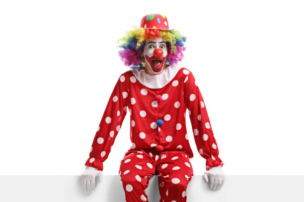 istock Funny clown sitting on a white billboard 1308641351