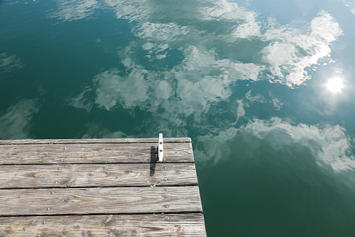 A weathered jetty dock - with an open row boat tied to one of its double cleat mooring bollards - is floating peacefully at water's edge on a harbor bay or lake in Nova Scotia, Canada.