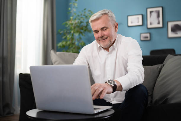 istock Smiling happy middle aged 50s old senior man using laptop computer technology working online, surfing internet, typing email, shopping in ecommerce store relaxing with device sitting on couch at home 1308643987
