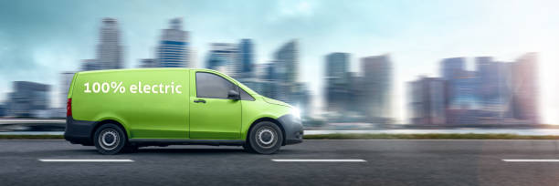 Driving electric van in front of a city skyline A modern van driving on a highway. There is text on the side of the van that reads "100% electric". Motion blurred background with a city skyline. energy fuel and power generation city urban scene stock pictures, royalty-free photos & images