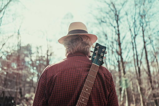 Vista trasera del hombre caminando por la carretera rural con la guitarra en la espalda photo