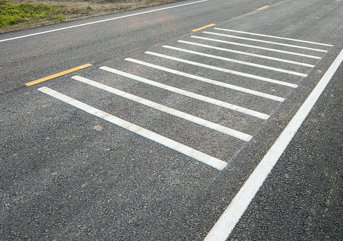 White transverse rumble strips on the asphalt road for causing a loud noise to alert the driver to be aware before reaching the intersection in the countryside village, front view with the copy space.