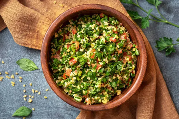 Traditional Arabic salad tabbouleh in a wooden bowl on a dark background top view. Arabic cuisine, vegan food.