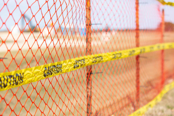 Close-up of yellow Caution tape on an orange mesh fence near a construction zone.