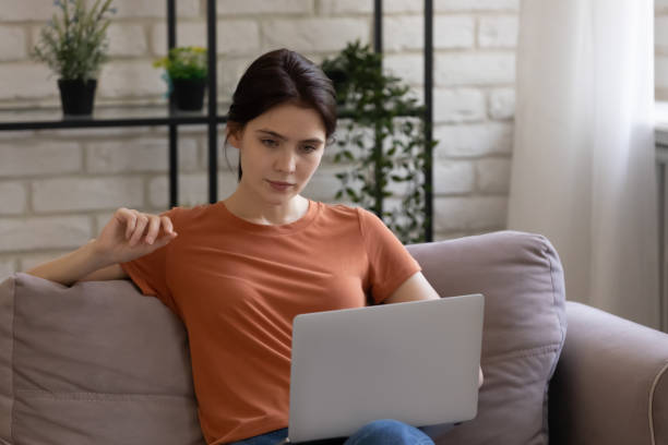 istock Serious woman using laptop, looking at screen, sitting on couch 1308658889
