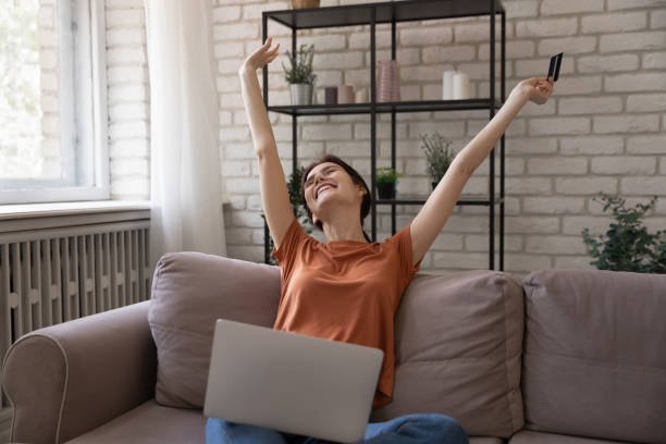 istock Overjoyed woman holding credit card, using laptop, celebrating great purchase 1308658899
