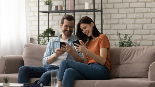 istock Overjoyed couple using phones together, sitting on cozy couch 1308658931