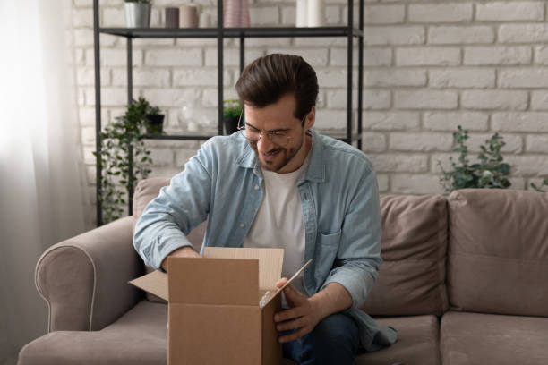 istock Curious young man unpacking awaited parcel, sitting on couch 1308658967