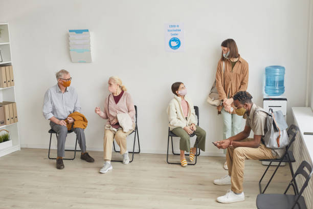 Group of People Waiting in Line at Clinic Wide angle view at hospital waiting room with diverse group of people waiting in line for vaccination, copy space waiting room stock pictures, royalty-free photos & images