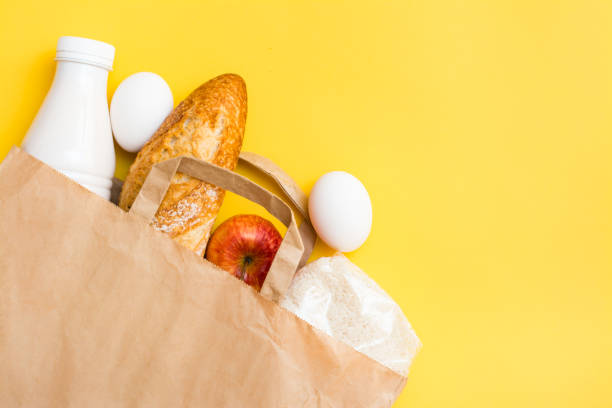 konzept der lebensmittellieferung. brot, milch, eier, getreide und früchte in einer papiertüte auf gelbem grund - milk bread stock-fotos und bilder