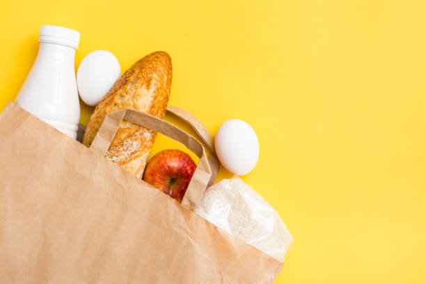 concepto de entrega de alimentos. pan, leche, huevos, cereales y frutas en una bolsa de papel sobre un fondo amarillo - milk bread fotografías e imágenes de stock
