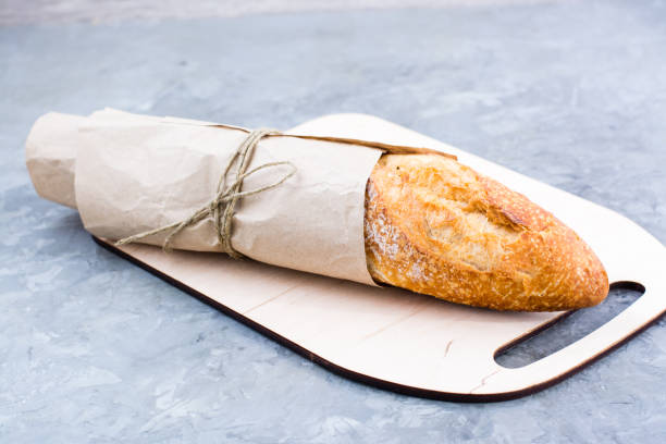 istock Fresh baguette in wrapping paper on cutting board on table 1308668325