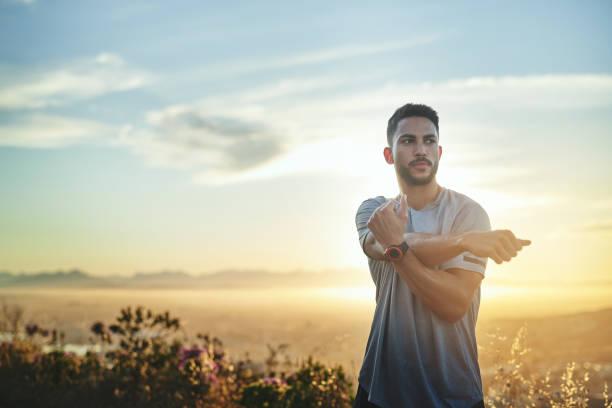 Shot of a young man stretching while out for a workout on a mountain road