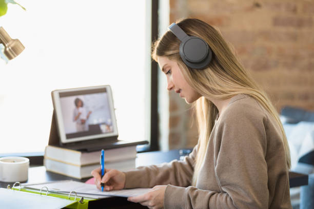 istock Female student with headphones takes notes during virtual class 1308679919