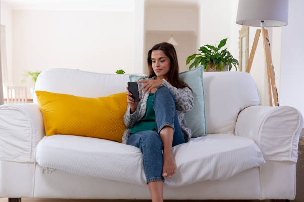 istock Caucasian woman sitting on a couch using smartphone and smiling 1308683707