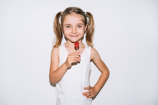 blonde girl with blue eyes very happy smiling with a lollipop in her hands on a white background