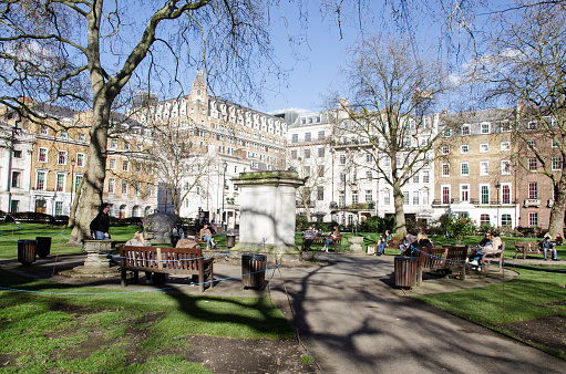 London, UK - February 26, 2021:  Workers enjoying a lunchtime break in the spring sunshine in Cavendish Gardens, Westminster, London on a sunny February afternoon.