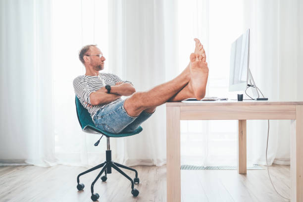 istock A middle-aged man in eyeglasses watching a modern computer in his living room. He put her barefoot lags on the table and relaxing. Video streaming on worldwide quarantine time concept 1308686635