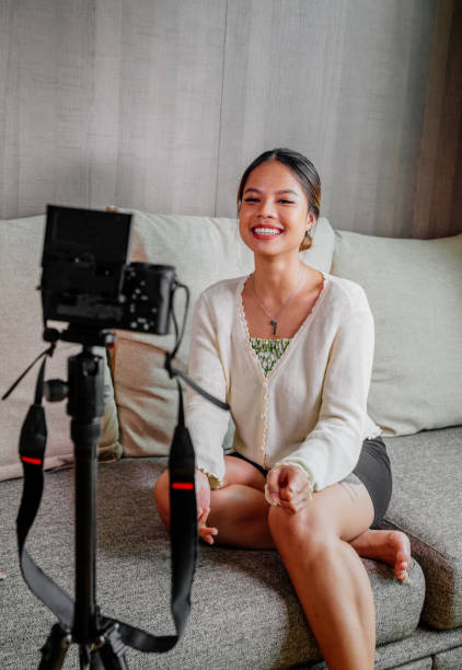 blogueiro asiático, podcaster ou vlogger olhando para a câmera e falando em vídeo filmando com tecnologia. pessoas influenciadoras de mídia social ou conceito de criador de conteúdo em relaxar estilo casual em casa - women home video camera camera vitality - fotografias e filmes do acervo