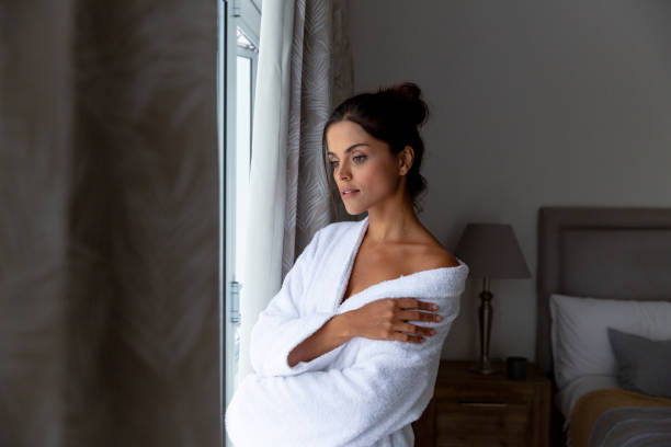 istock Caucasian woman wearing bathrobe standing by a window and smiling 1308689019