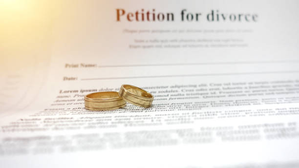 Conceptual image for divorce with two golden wedding ring in the middle and petition for divorce as background. Main focus on the rings. stock photo