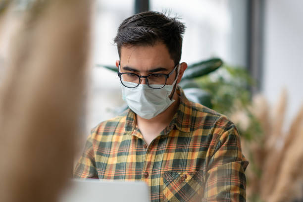 istock Man with face mask working on laptop in cafe 1308694857