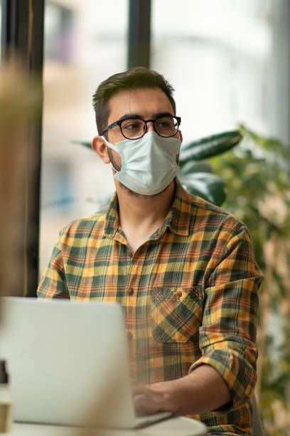 istock Man with face mask working on laptop in cafe 1308694916