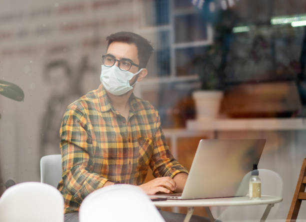 istock Man with face mask working on laptop in cafe 1308694970