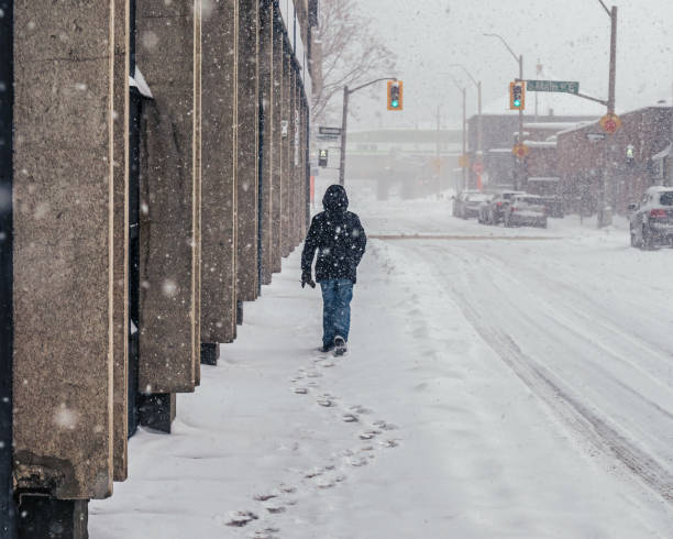istock Person Walking away in a Snowstorm with footprints 1308701626