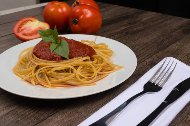 istock Pasta with sugo sauce and basil leaves. Whole red tomatoes. Tomato sliced half at the bottom. Cutlery on napkin. Popular food photography 1308703870