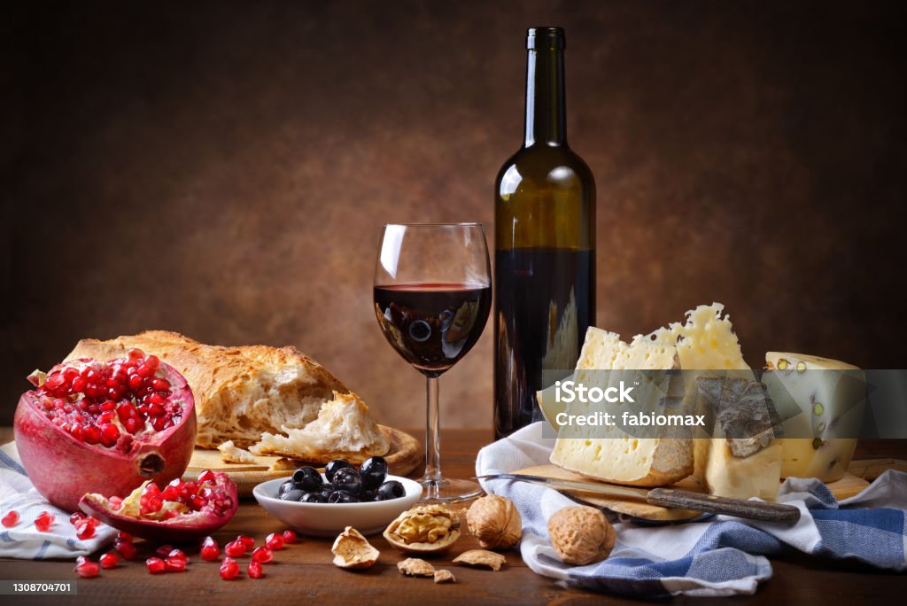 Red wine, cheese, walnuts, olives, pomegranate and bread. Rustic meal, copy space. Cheese Board Stock Photo
