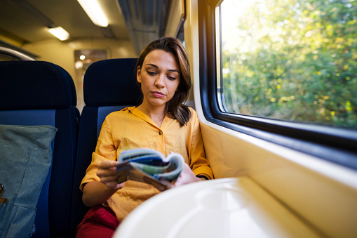 Front view of a young Caucasian woman riding on the train while reading her book.