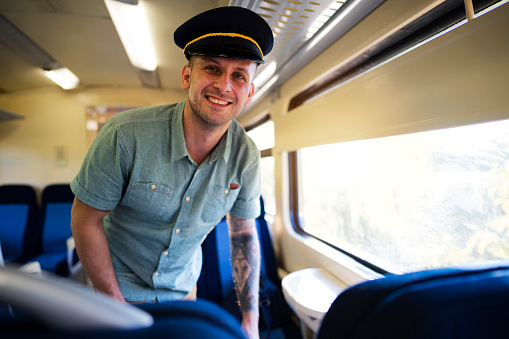 Young Caucasian man enjoying his railroad ride whit a funny train conductor's hat and looking at the camera.