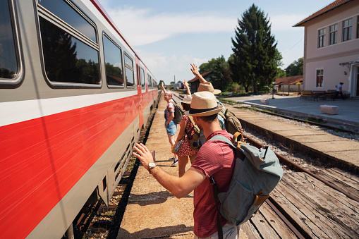 Small group of young Caucasian people having fun at the train station and waving at the passengers.