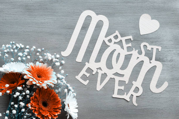 Mothers day greeting card design. Gerberas and white baby breath flowers on grey wood background. Flower arrangement, floral composition. Paper text Best Mom Ever. Happy Mother's day. Monochrome image diseño de tarjeta de felicitación del día de las madres. gerberas y flores blancas de aliento de bebé sobre fondo de madera. arreglo floral, composición floral. texto en papel mejor mamá de la historia. feliz día de la madre. imagen monocromática
