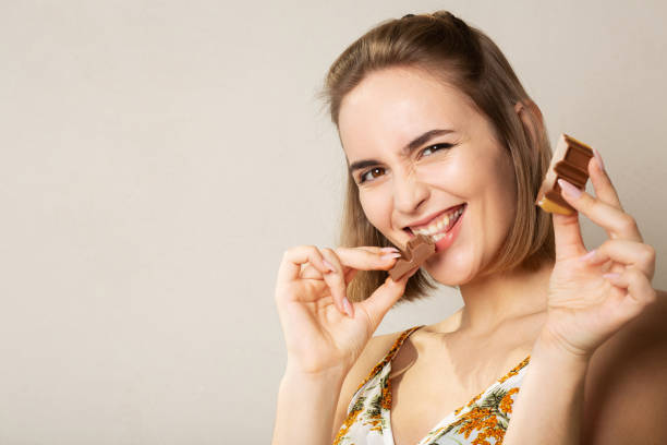 istock Pretty cheerful woman eats milk chocolate posing on a grey studio background 1308719287