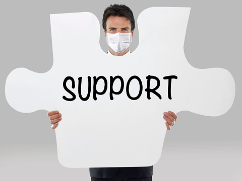 Businessman wearing a mask holding a missing piece of a puzzle with “Support” text