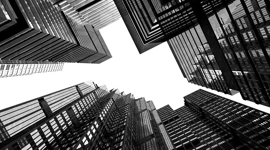 Tall skyscrapers and high rise buildings seen from below, looking up. Glass windows and geometric patterns. Black and white image with monochrome style. White sky and neutral background. Digitally generated image.