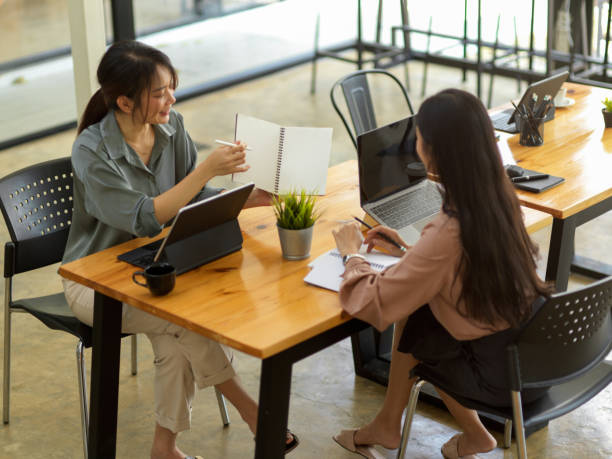 istock Two female office workers talking to each other while working together in meeting room 1308758448