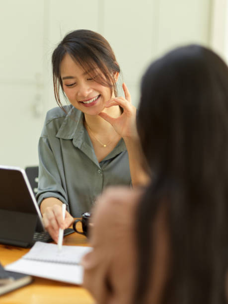 istock Smiling female workers talking with colleague and pointing on blank notebook 1308758665