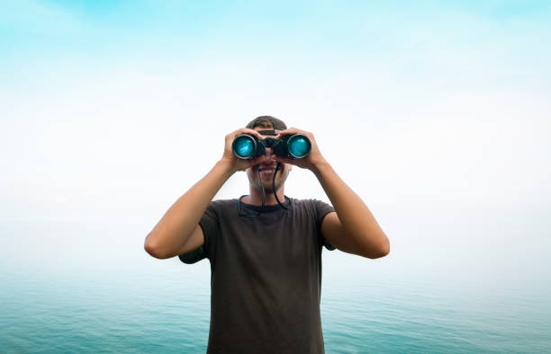 man with binoculars looking forward through the fog - looking at view water sea blue imagens e fotografias de stock