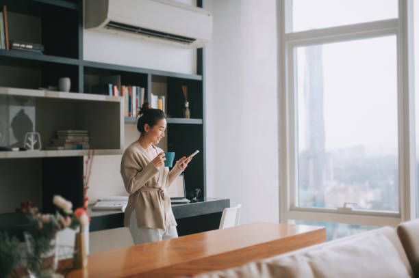 asiatische chinesische schöne frau genießen ihren nachmittagstee im wohnzimmer blick nach draußen fenster entspannen auf dem tisch lehnen - living room people joy happiness stock-fotos und bilder