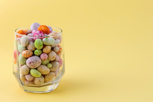 glass cup with colored candies on a yellow background with a copy of the space.